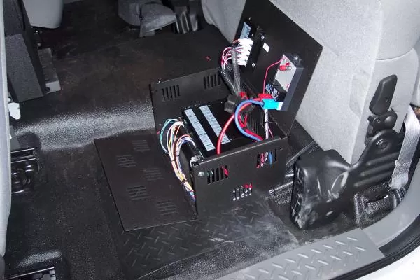 Lid open on the floor-mounted box, revealing the fuse block, relays and bundled wiring harness inside