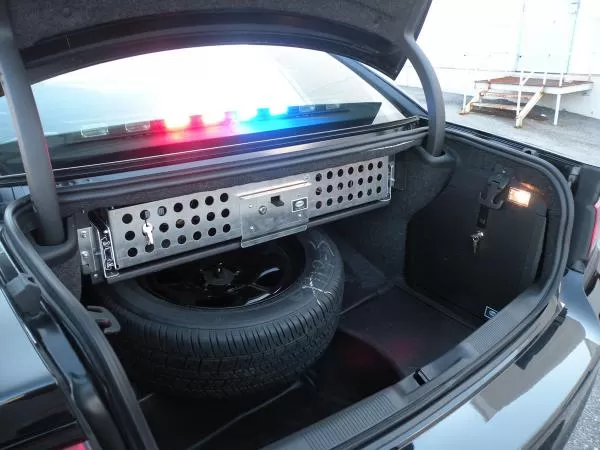 Trunk interior with the perforated aluminum equipment panel mounted above the spare tire, lightbar lit