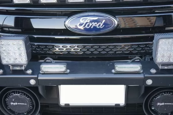 Slim modules mounted on the licence plate bar of a Ford grille between two larger LED lamps