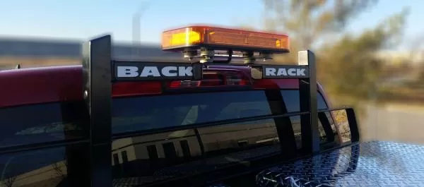 Amber bar flashing on a BACK RACK headache rack behind the cab of a red pickup truck