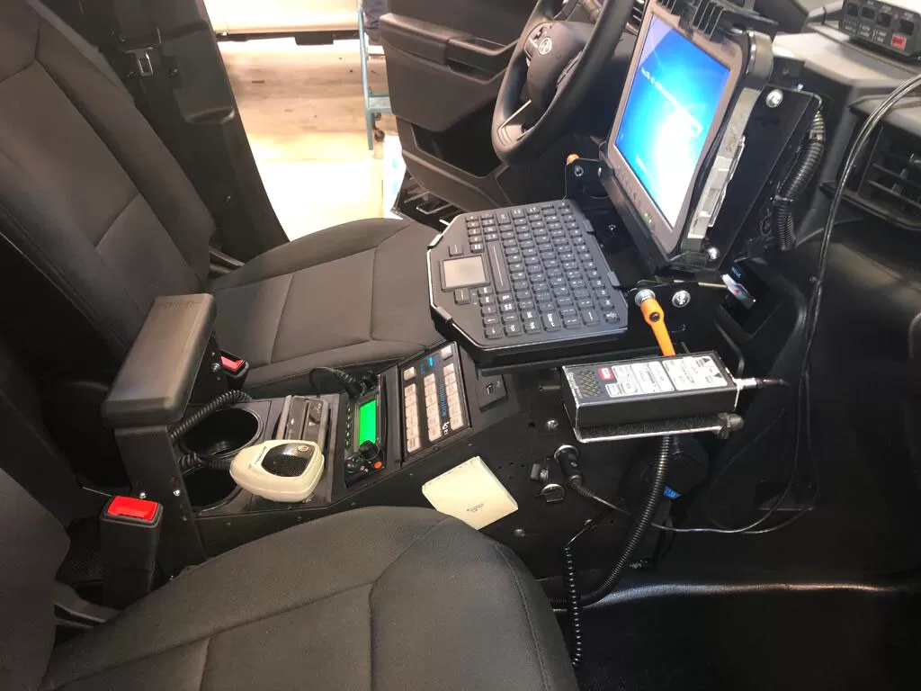 Driver-side view of the installed console carrying a siren controller, radio faceplates and a docked laptop