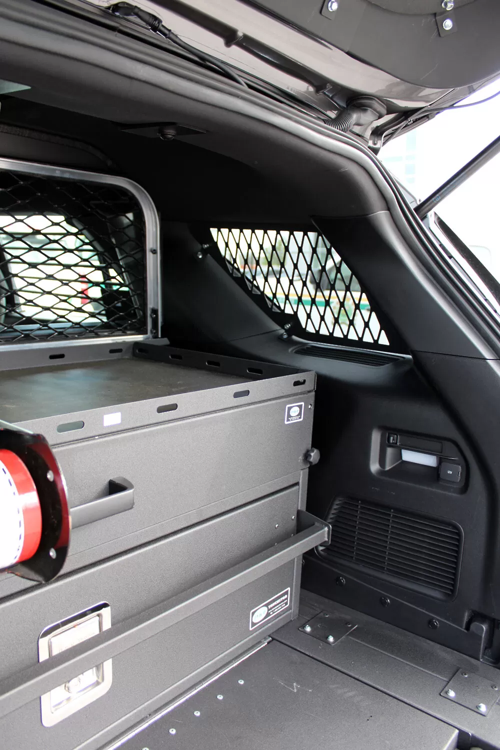 Quarter-window mesh screen above a two-drawer storage unit in the cargo area of an upfitted SUV