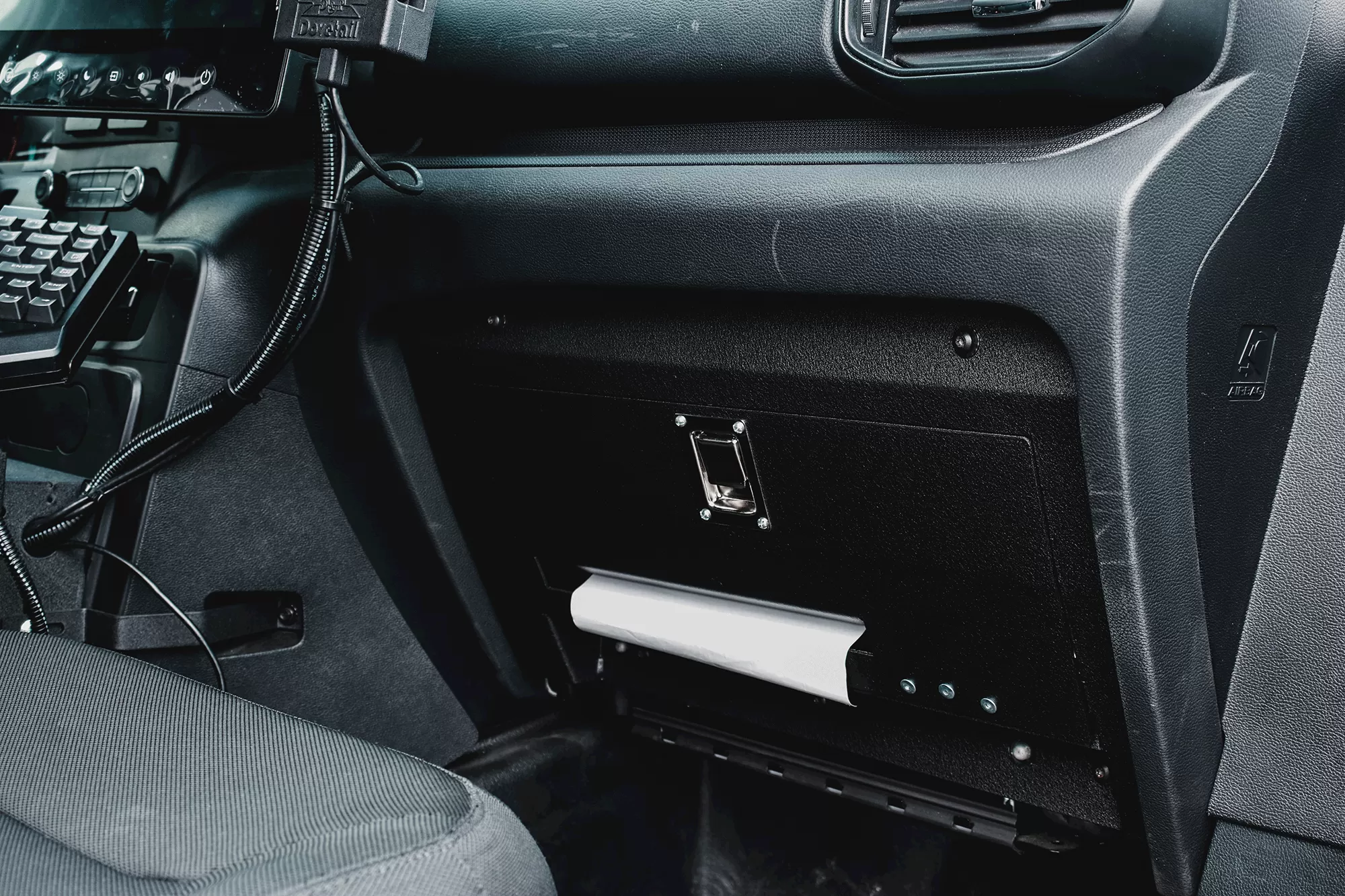 Closed glove box faceplate with chrome latch above an open shelf holding a white paper roll
