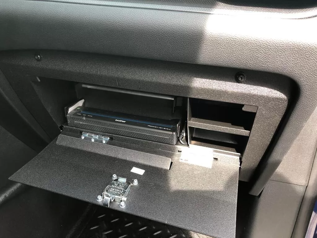 Angled close-up of a Brother printer seated in the open glove box with the latch on the inside of the door