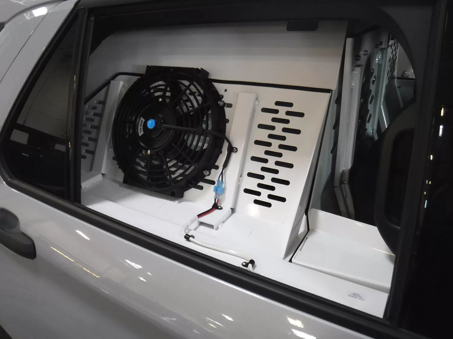 Black ventilation fan and wiring mounted inside the kennel, seen through the rear side window