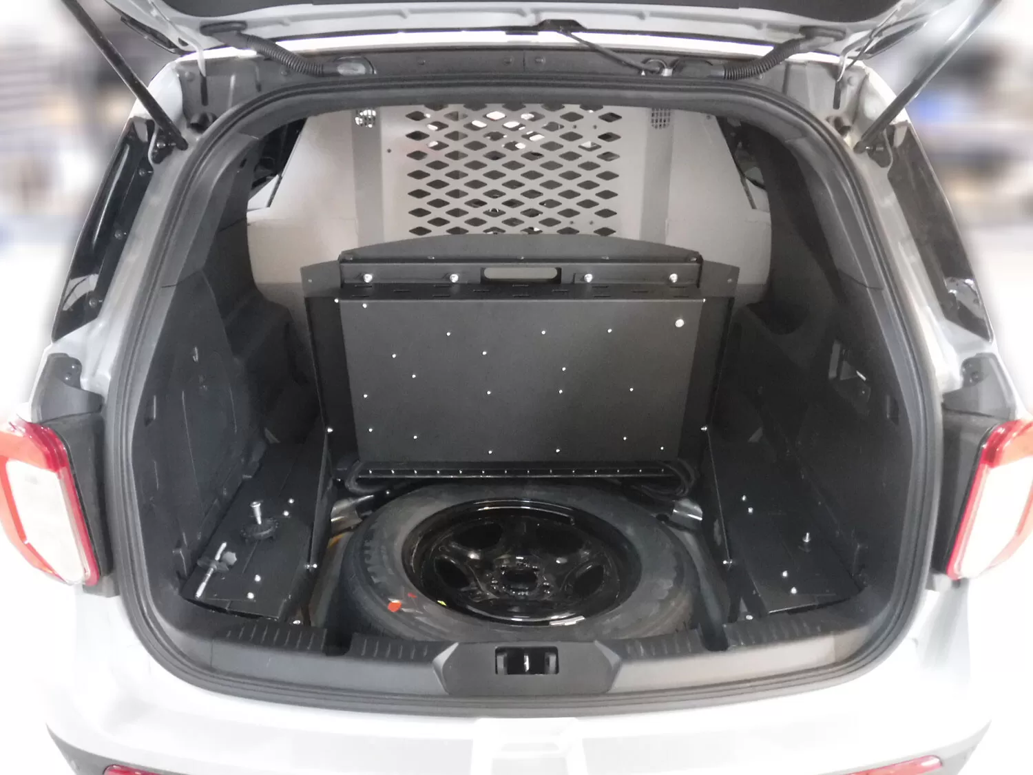 Hinged black rear panel raised in the cargo area to expose the spare tire behind the dog compartment