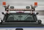 Amber light stick lit on the cab rack of a white truck between two rotating beacons and work lights