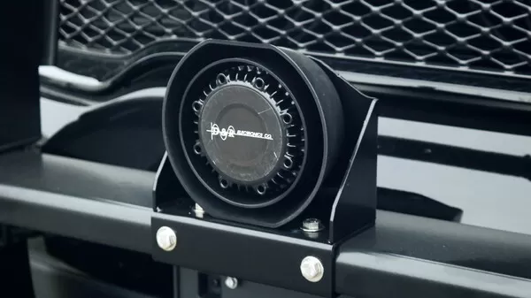 Speaker bolted to a black bracket on a push bumper directly in front of a vehicle grille