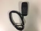 Handheld touchpad lying beside its coiled cord and modular plug on a bench