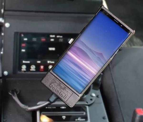 Phone docked in a cruiser console beside a red-lit radio faceplate, cable running from the dock base