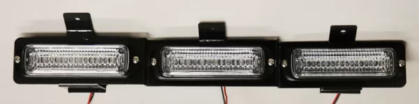 Bare three-module assembly on its black mounting bracket with wiring pigtails, straight-on and unlit