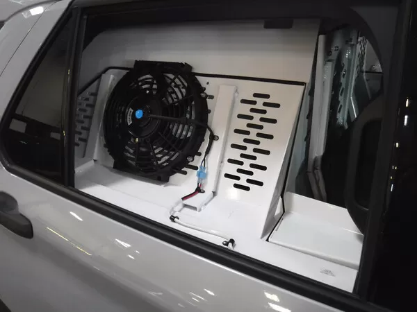 Black ventilation fan and wiring mounted inside the kennel, seen through the rear side window